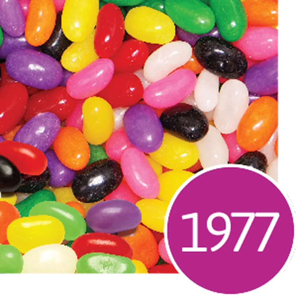 A collection of multi-colored jelly beans with a purple circle showing the number 1977 in the bottom right corner.