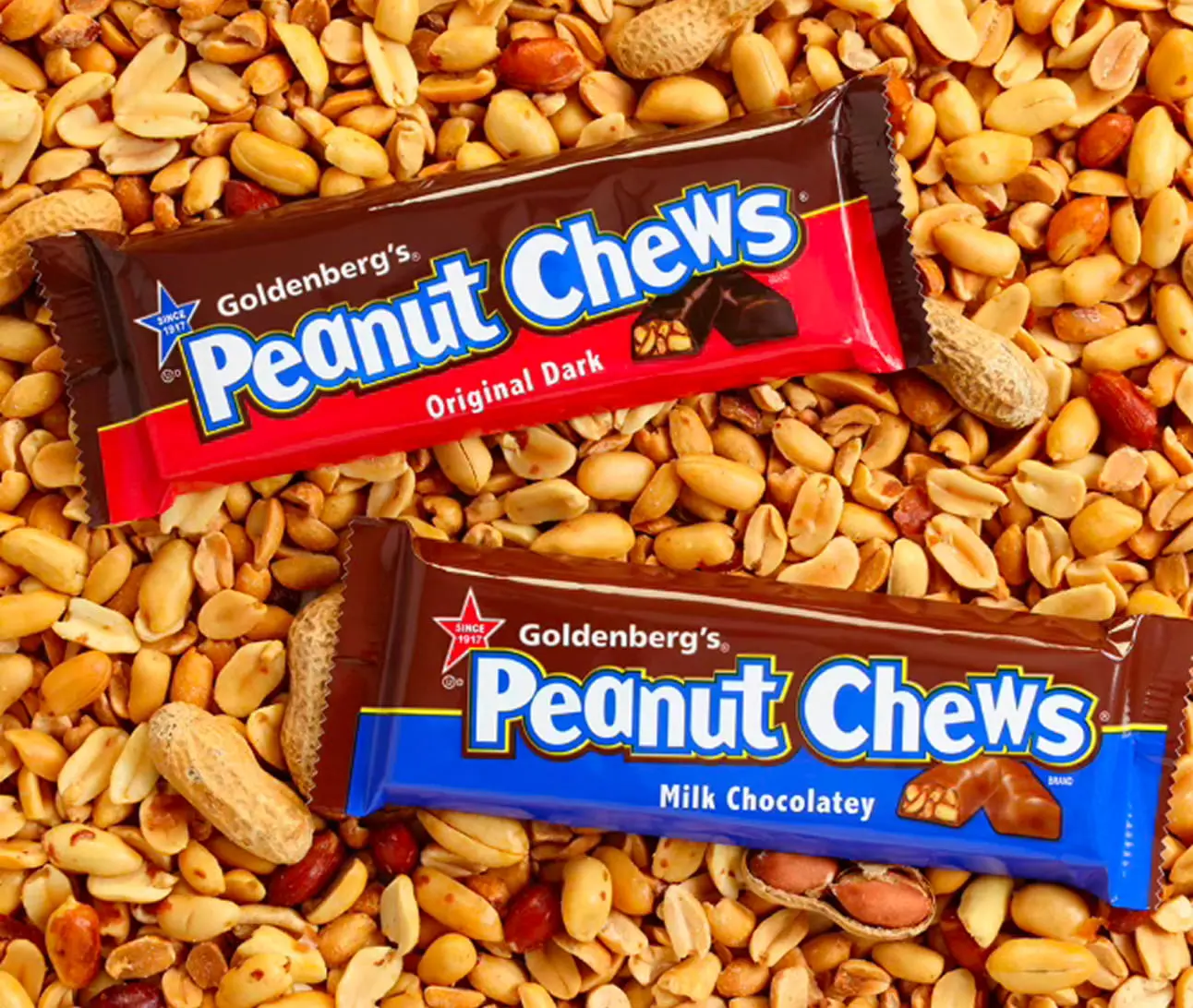 Two Goldenberg’s Peanut Chews candy bars rest on a dense bed of shelled and unshelled peanuts.
