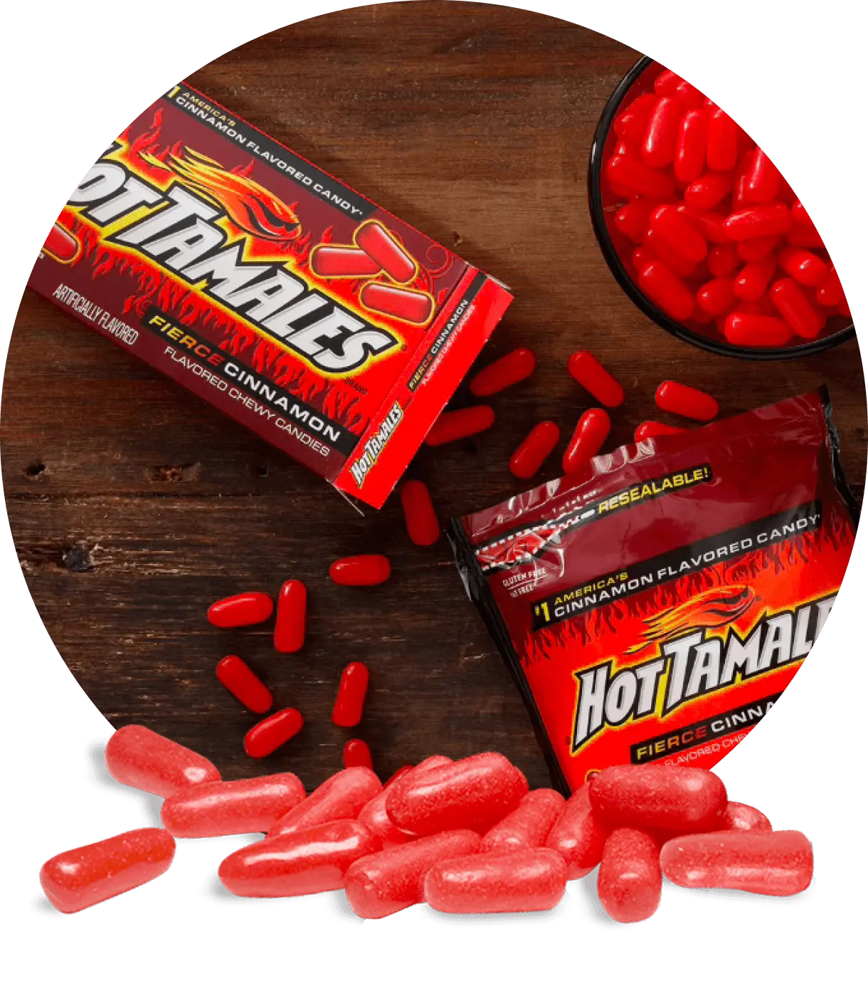 A box and a bag of Hot Tamales Fierce Cinnamon candies on a wooden table, with loose red candies in a bowl and scattered around.