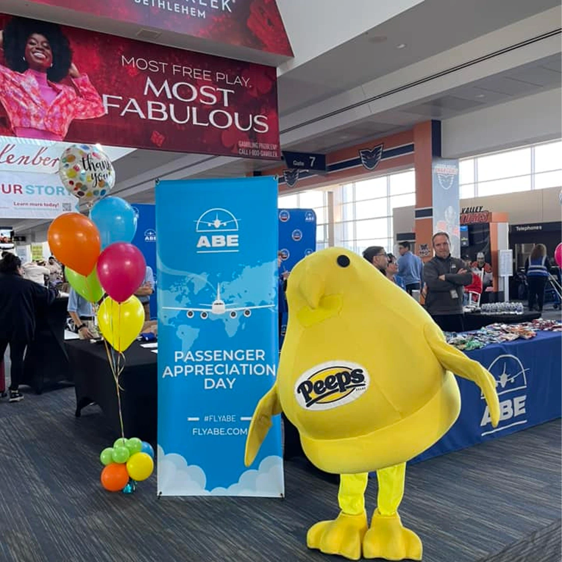 A yellow Peeps mascot stands next to a "Passenger Appreciation Day" banner and colorful balloons